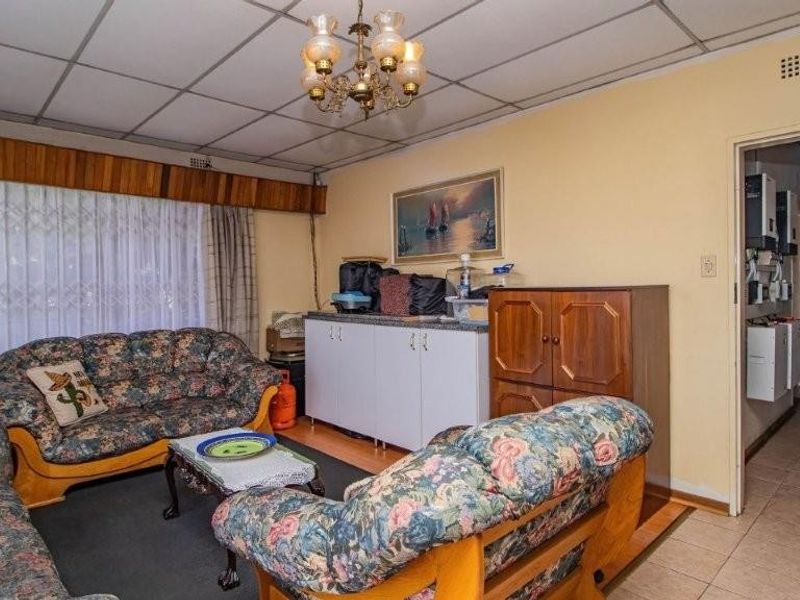 A dated living room featuring a drop ceiling, tiled flooring in the adjacent hallway, and access to internal living spaces.