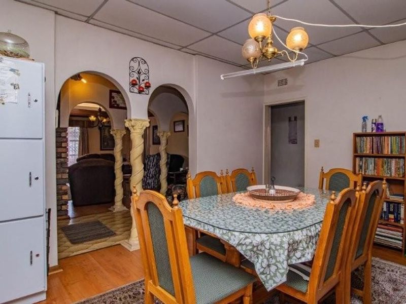 Dining area featuring a drop ceiling, decorative archways with columns, and wood-look flooring, providing a traditional layout with access to adjacent living spaces.