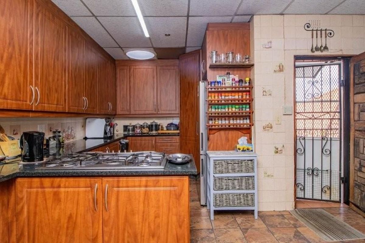 A functional kitchen featuring wood-finish cabinetry, granite countertops, a built-in gas hob, and direct access to an exterior security gate.