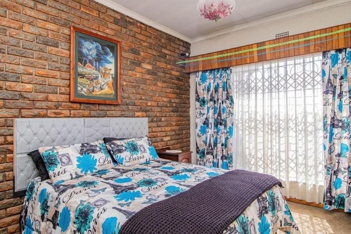 A bedroom featuring a prominent exposed brick feature wall, large window with security gate, and neutral carpeting.