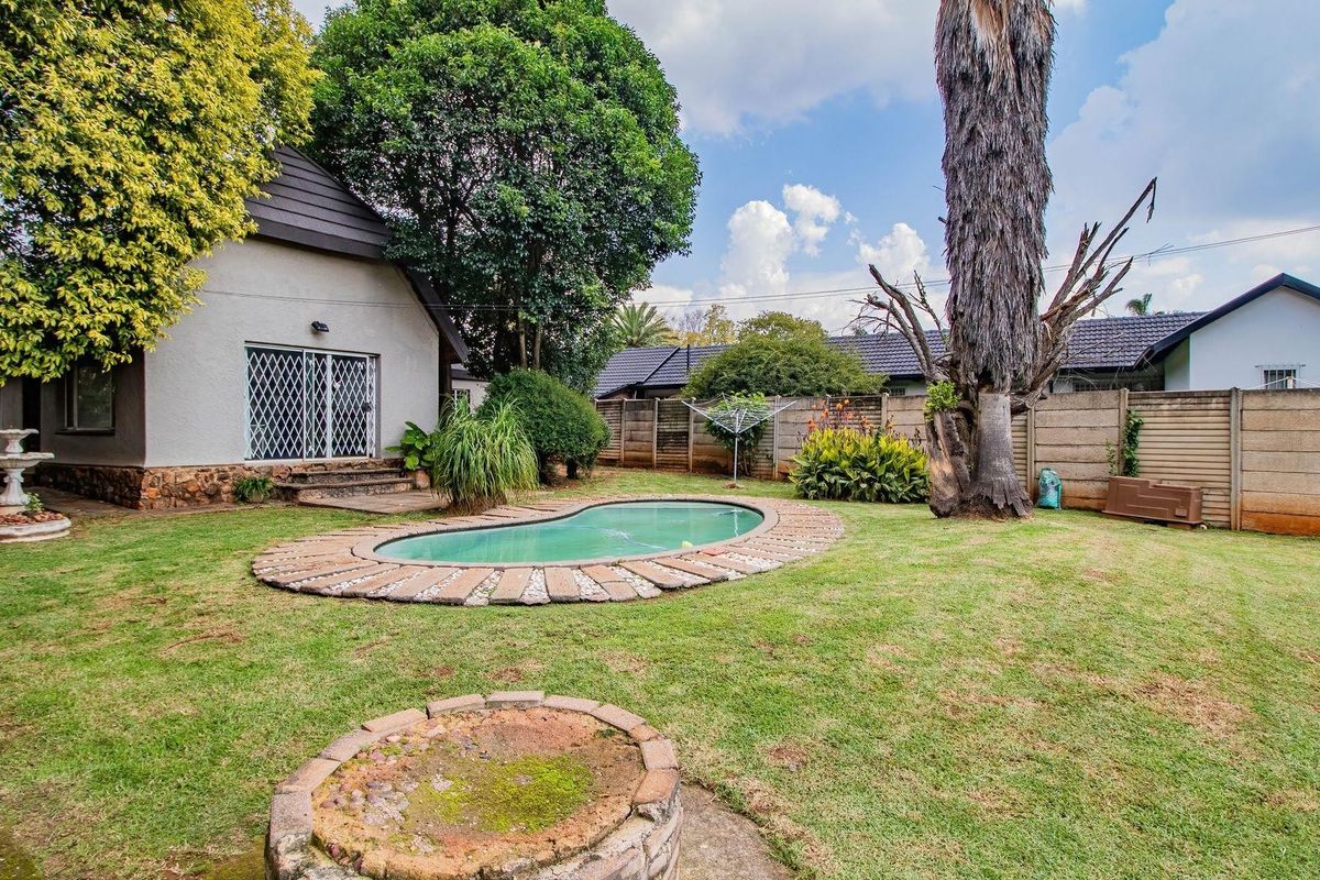 Spacious rear garden featuring a kidney-shaped swimming pool, paved surround, established trees, and a brick fire pit area.