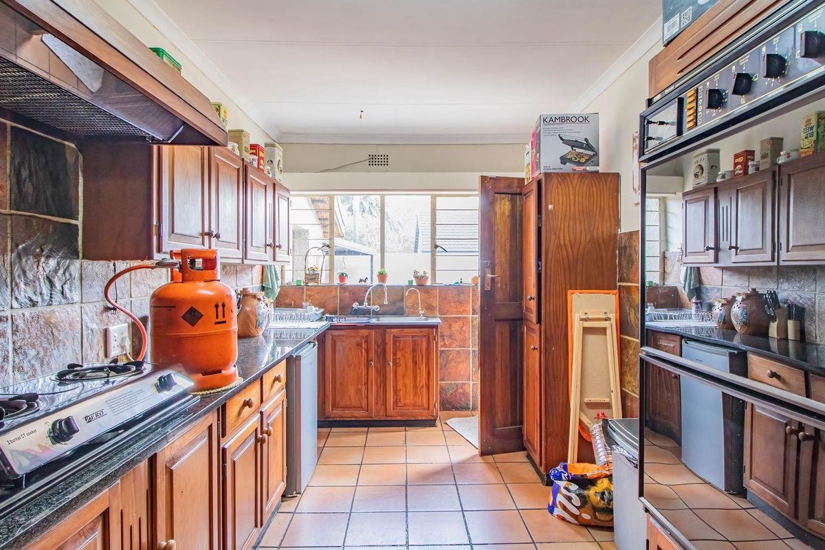 A functional kitchen featuring wooden cabinetry, dark stone countertops, tiled flooring, and a built-in oven, offering a traditional aesthetic with ample storage space.