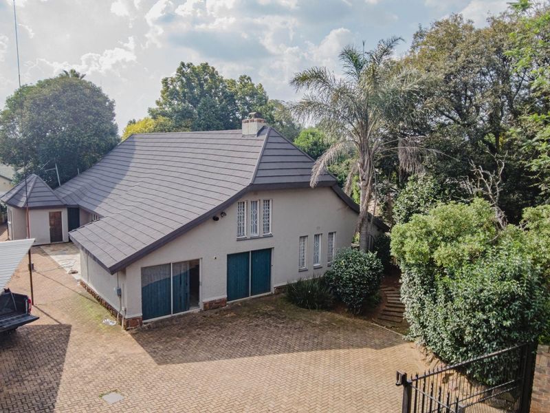 Aerial view of the property featuring a tiled roof, paved driveway, carport, and established garden surroundings.