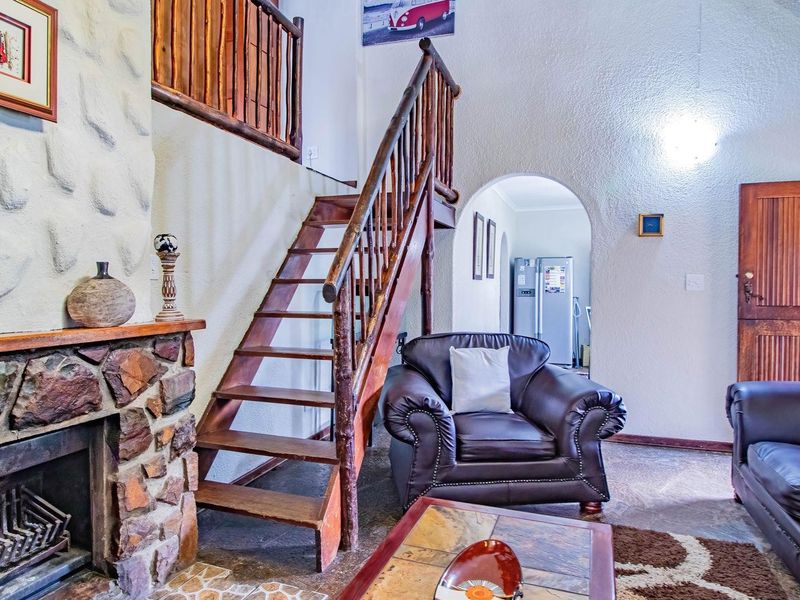 Living room featuring a rustic stone fireplace, wooden staircase with log-style railing, and arched doorway leading to the kitchen area.