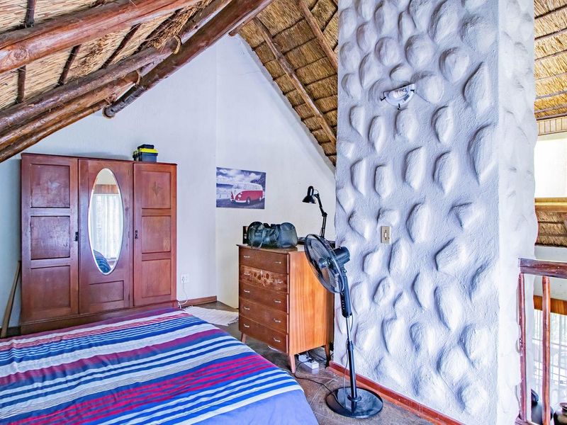 A rustic bedroom featuring a unique textured stone feature wall, exposed timber rafters, and a traditional thatched roof design.