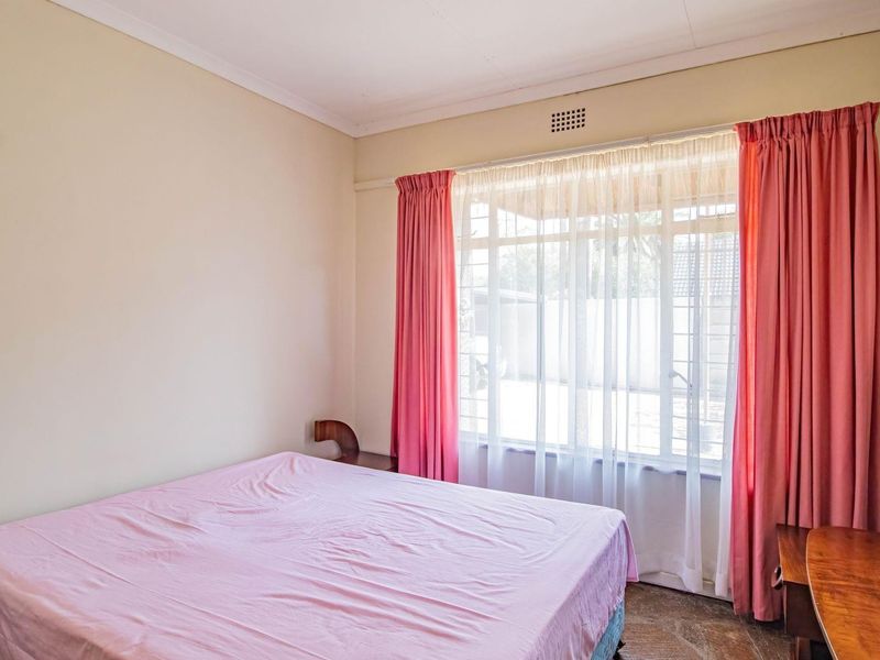 A bedroom featuring a large window with natural light, neutral wall finishes, and tiled flooring.