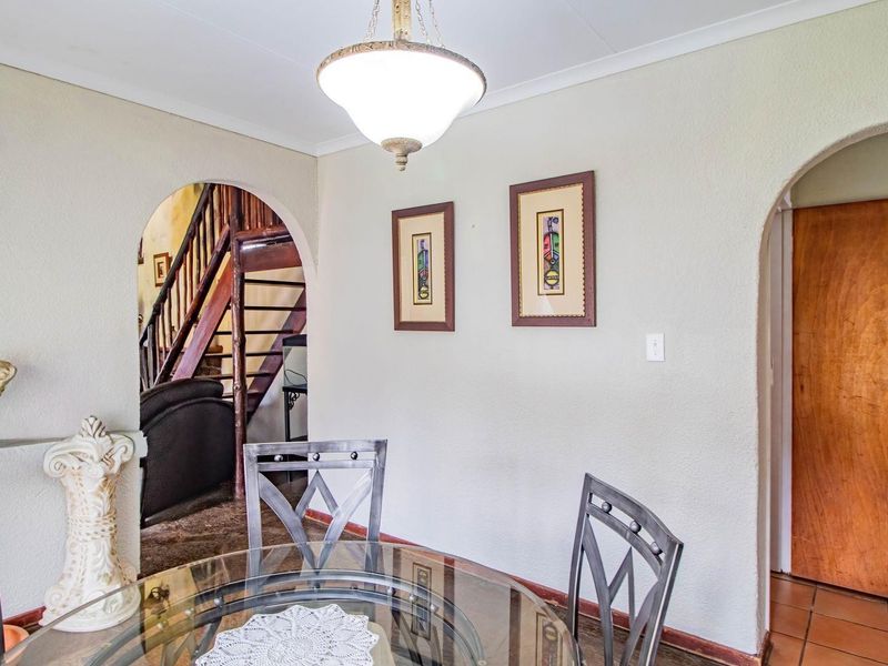 A dining area featuring arched doorways, a central pendant light fixture, and tiled flooring, with a view through to a staircase.