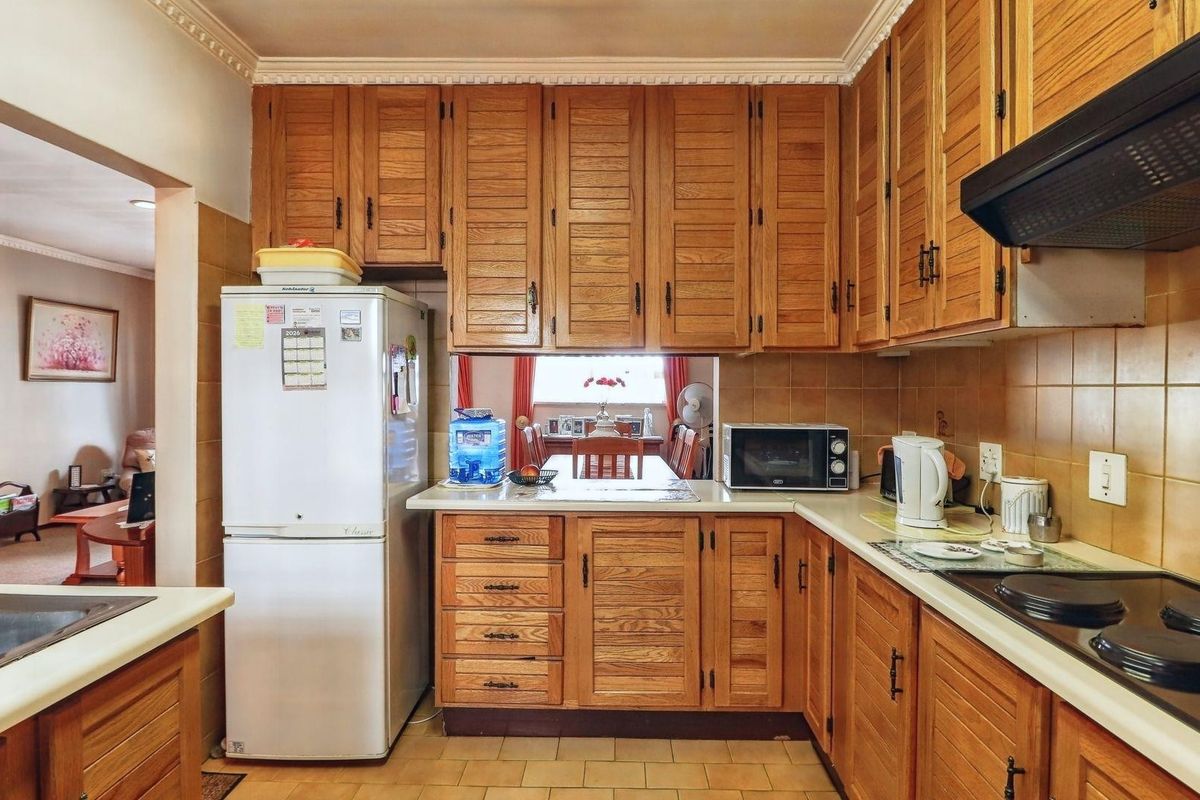 A functional kitchen featuring traditional timber cabinetry, tiled splashbacks, a built-in hob, and an extractor fan, with a convenient serving hatch to the dining area.