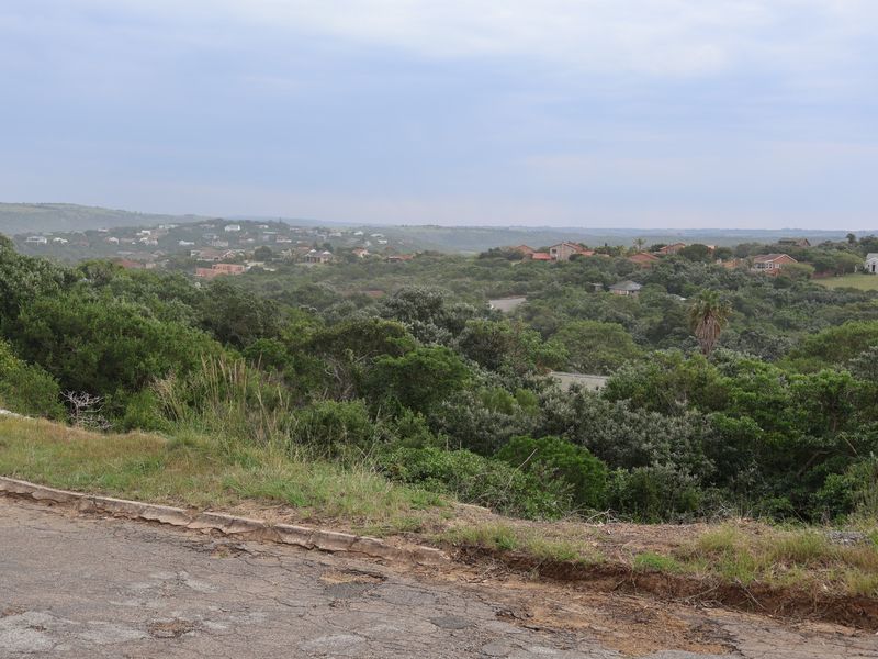 A scenic view overlooking a lush, green landscape with residential properties nestled in the distance, captured from an elevated road position.