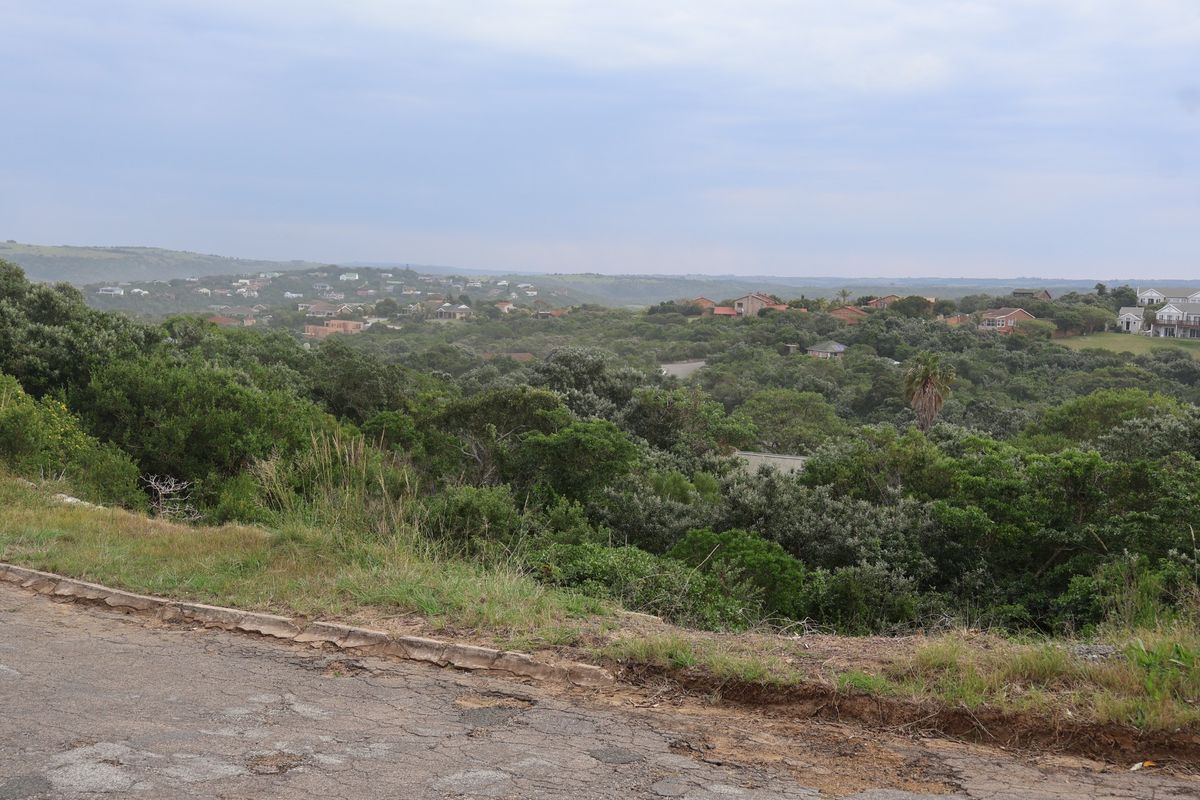 A scenic view overlooking a lush, green landscape with residential properties nestled in the distance, captured from an elevated road position.