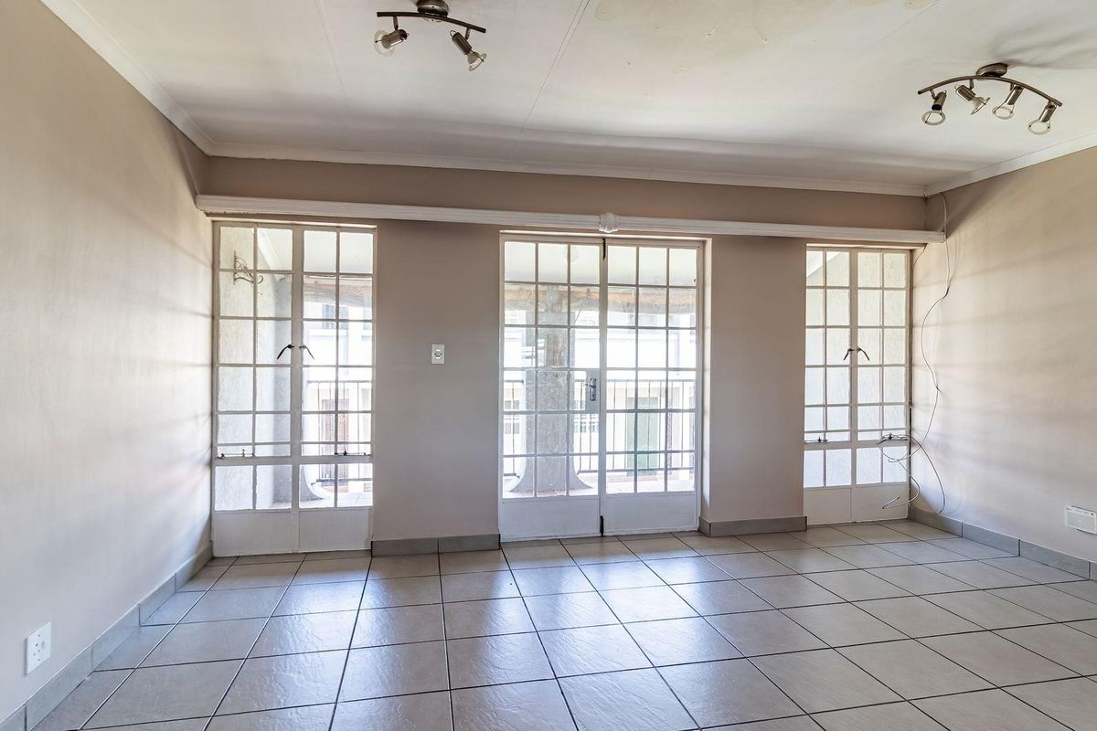 Spacious living area featuring neutral tiled flooring, dual ceiling-mounted spotlights, and multiple glass-paned doors providing access to the exterior.