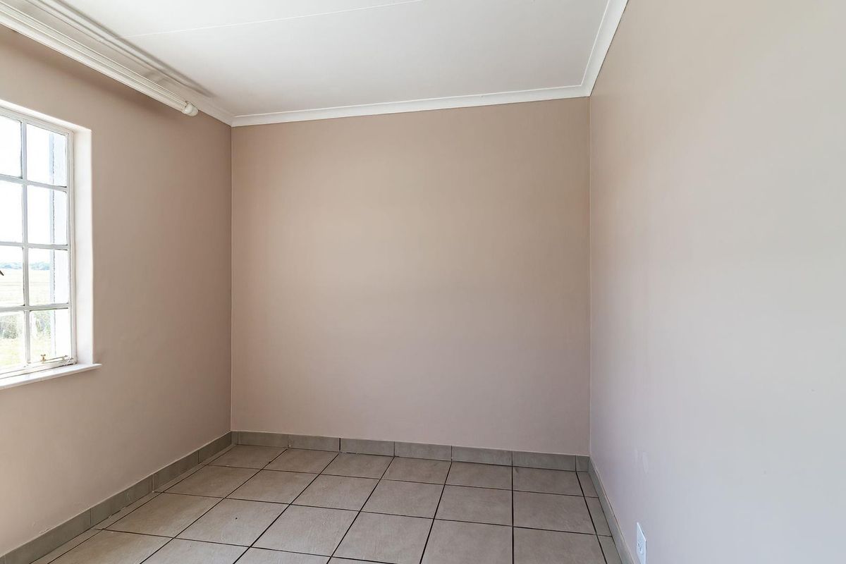 A simple, empty bedroom featuring neutral wall paint, tiled flooring, and a window providing natural light.