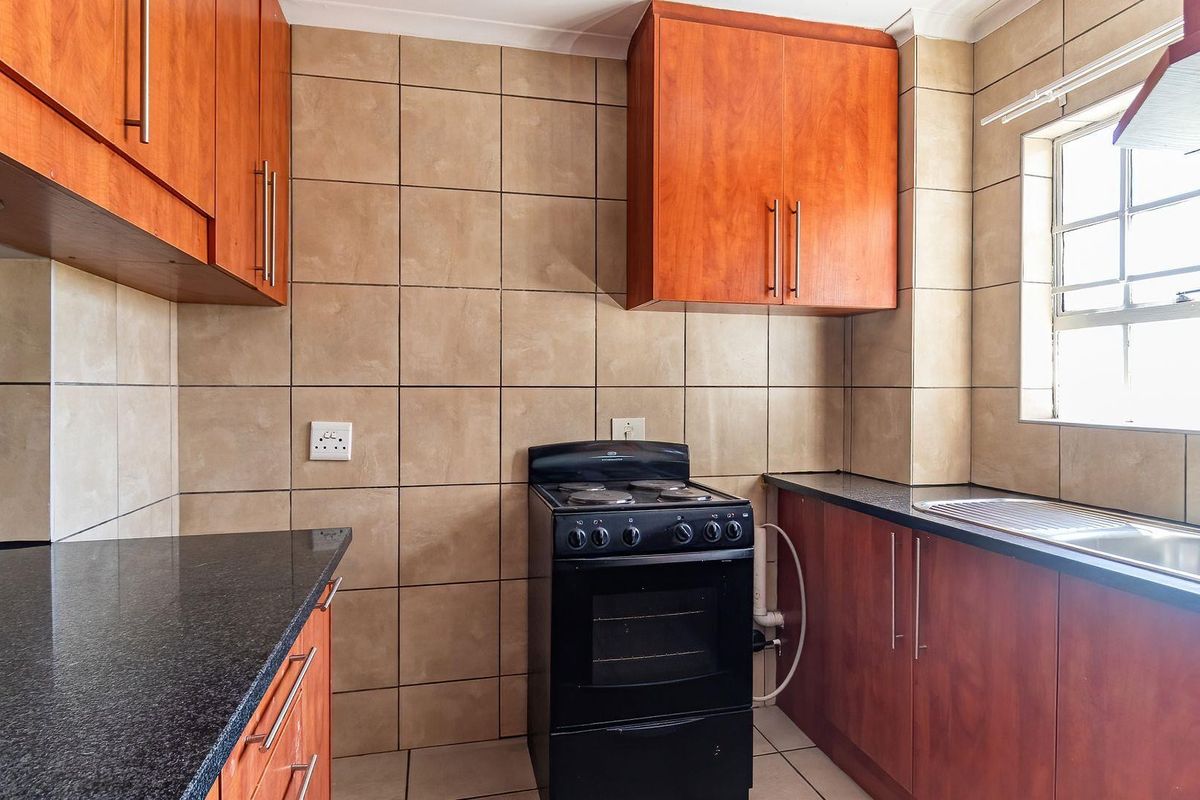 A functional kitchen featuring wooden cabinetry, dark granite-style countertops, a built-in stove, and tiled splashbacks with a window for natural light.