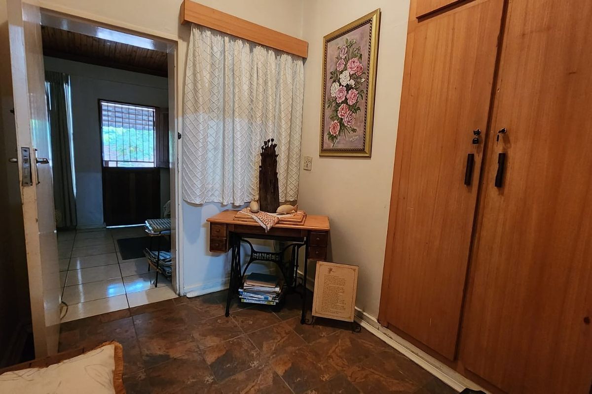 A bedroom featuring built-in wooden cupboards and tiled flooring, with a doorway leading to an adjacent living area.
