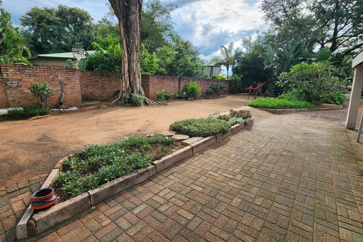 A spacious rear garden area featuring paved walkways, established garden beds with concrete edging, and a high brick boundary wall.