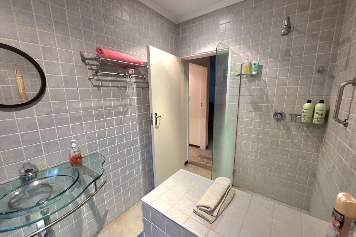A functional bathroom featuring a glass vessel sink, a tiled shower enclosure with a glass screen, and wall-mounted towel storage.