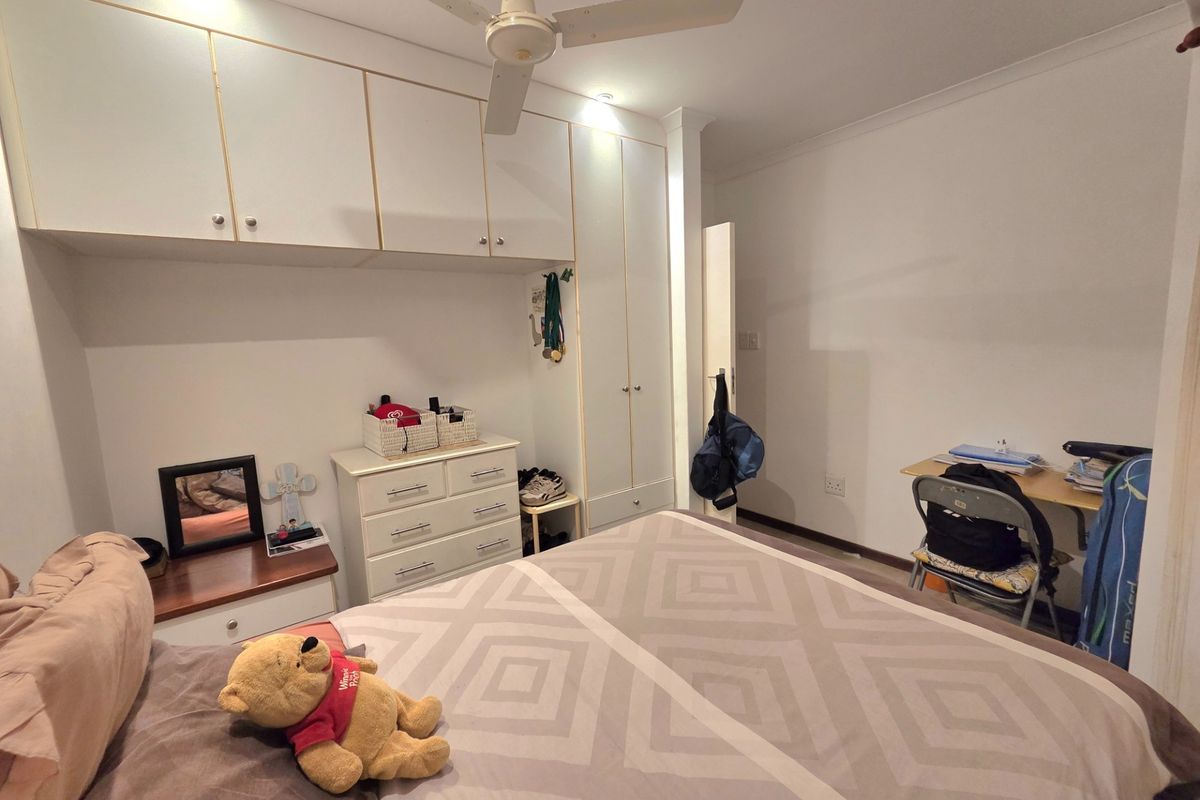 A bedroom featuring built-in white cabinetry, overhead storage cupboards, and a ceiling fan.