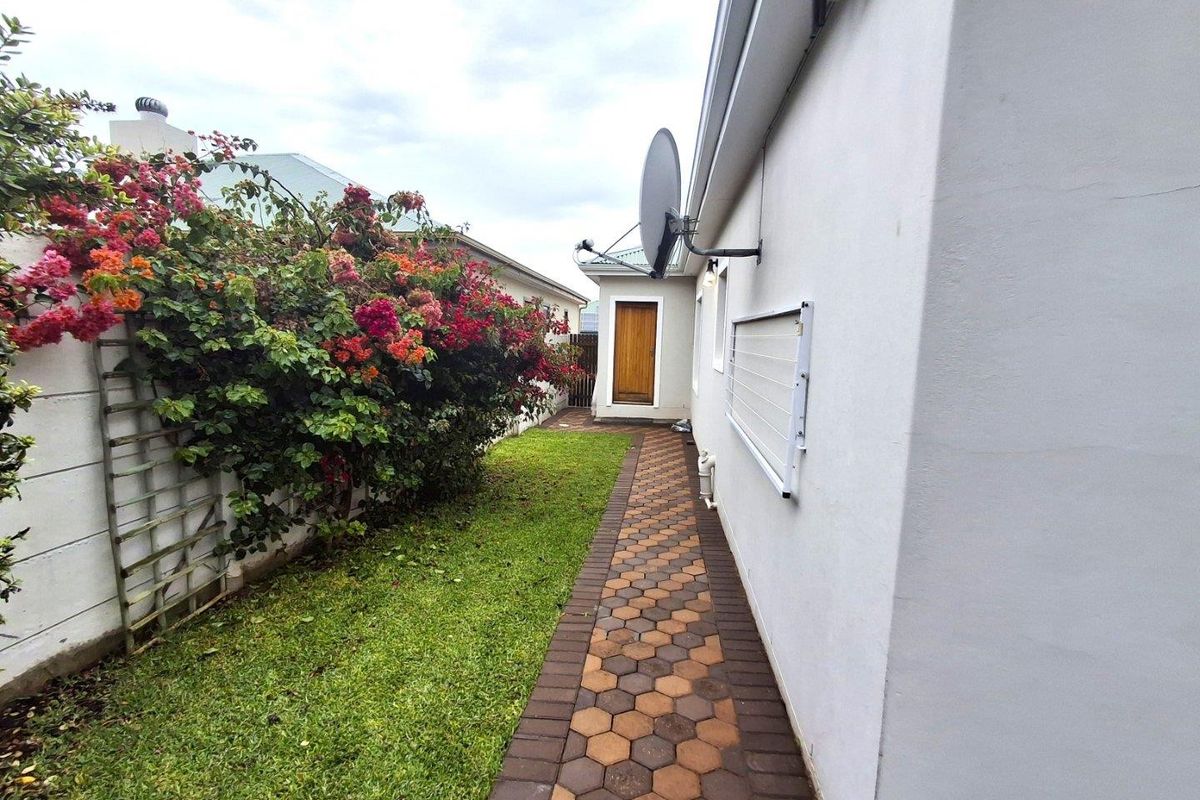 A side exterior walkway featuring a paved path, a wall-mounted clothesline, and a landscaped garden area with a boundary wall.