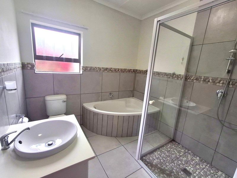 A modern bathroom featuring a corner bathtub, a glass-enclosed shower with pebble-style flooring, and a vanity basin.
