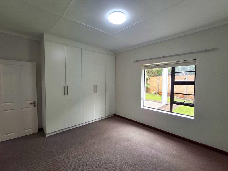 A clean, well-maintained bedroom featuring neutral carpeting, built-in floor-to-ceiling wardrobes, and a large window overlooking the rear garden.