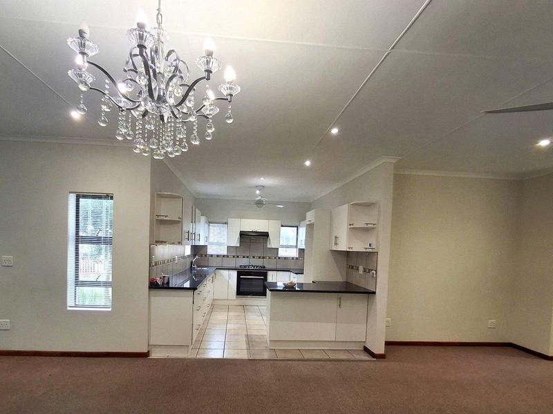 Open plan kitchen featuring white cabinetry, dark countertops, built-in oven, and extractor fan, seamlessly flowing into the adjacent living area.