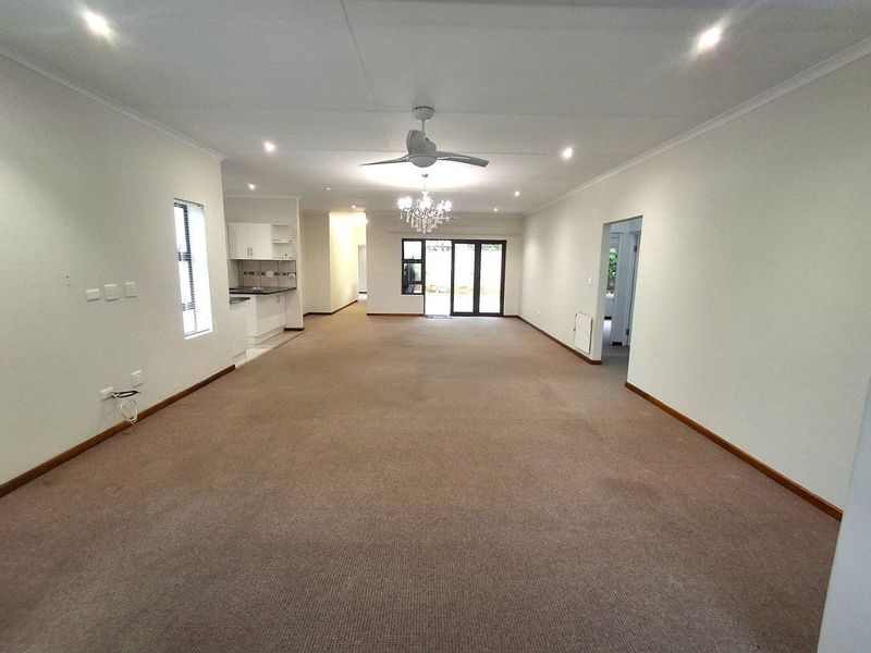 Spacious open-plan living area featuring neutral carpeting, recessed downlighting, a ceiling fan, and direct access to the rear exterior through sliding glass doors.