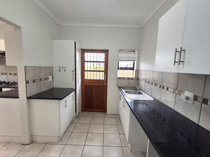 Functional kitchen featuring white cabinetry, dark granite countertops, tiled backsplash, and a wooden exterior door with security gate.