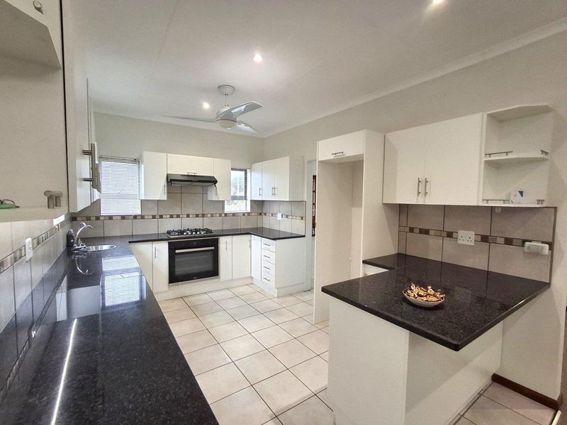 A functional kitchen featuring white cabinetry, dark granite countertops, tiled backsplash, built-in oven, gas hob, and an extractor fan.
