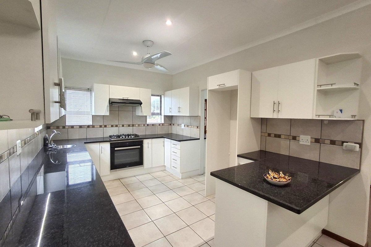 A functional kitchen featuring white cabinetry, dark granite countertops, tiled backsplash, built-in oven, gas hob, and an extractor fan.