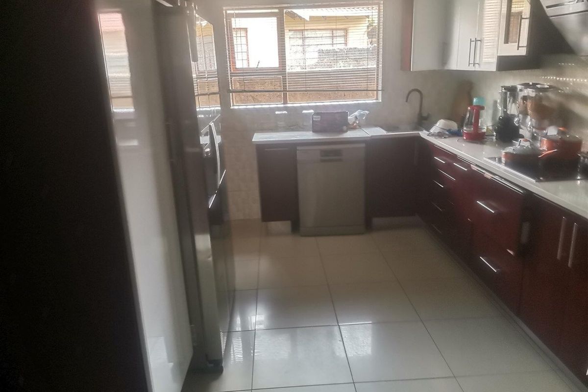 A functional kitchen featuring dark cabinetry, white countertops, tiled flooring, and an integrated dishwasher, offering a clean and practical workspace.
