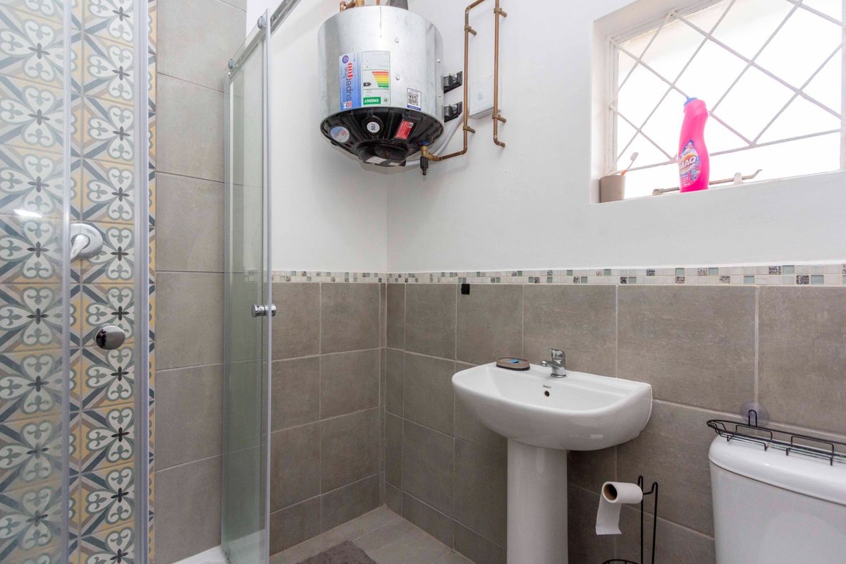 A functional bathroom featuring a glass-enclosed shower, pedestal basin, toilet, and wall-mounted electric water heater with tiled wall finishes.