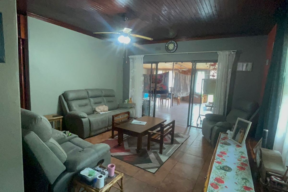 A living room featuring a dark wood-paneled ceiling, tiled flooring, and sliding glass doors that open onto an adjacent patio area.