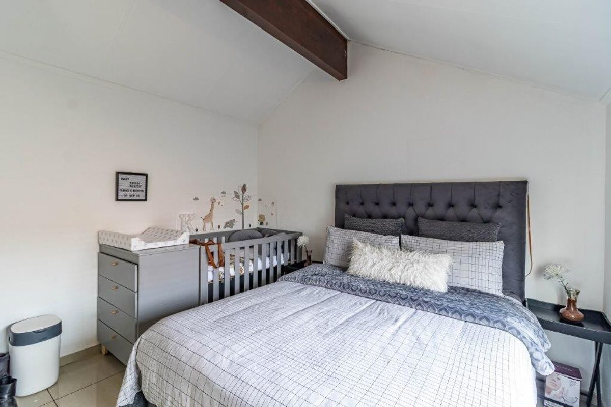 A well-maintained bedroom featuring a vaulted ceiling with an exposed timber beam, tiled flooring, and neutral wall finishes.
