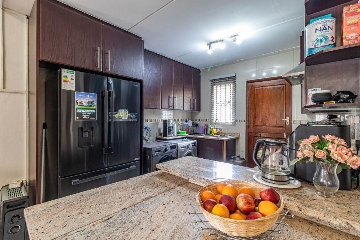 A functional kitchen featuring dark wood cabinetry, granite countertops, a breakfast bar, and integrated laundry appliances.