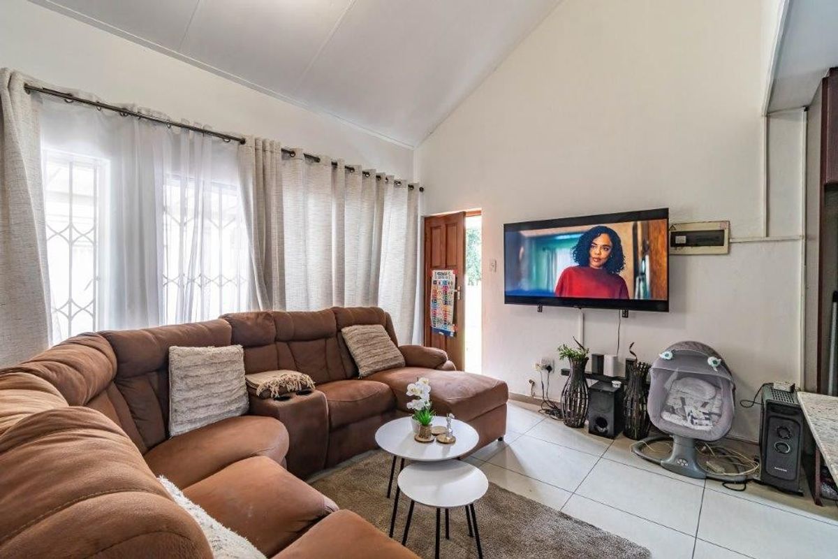 A living room featuring high vaulted ceilings, tiled flooring, and a wall-mounted television, providing a bright and functional space for relaxation.