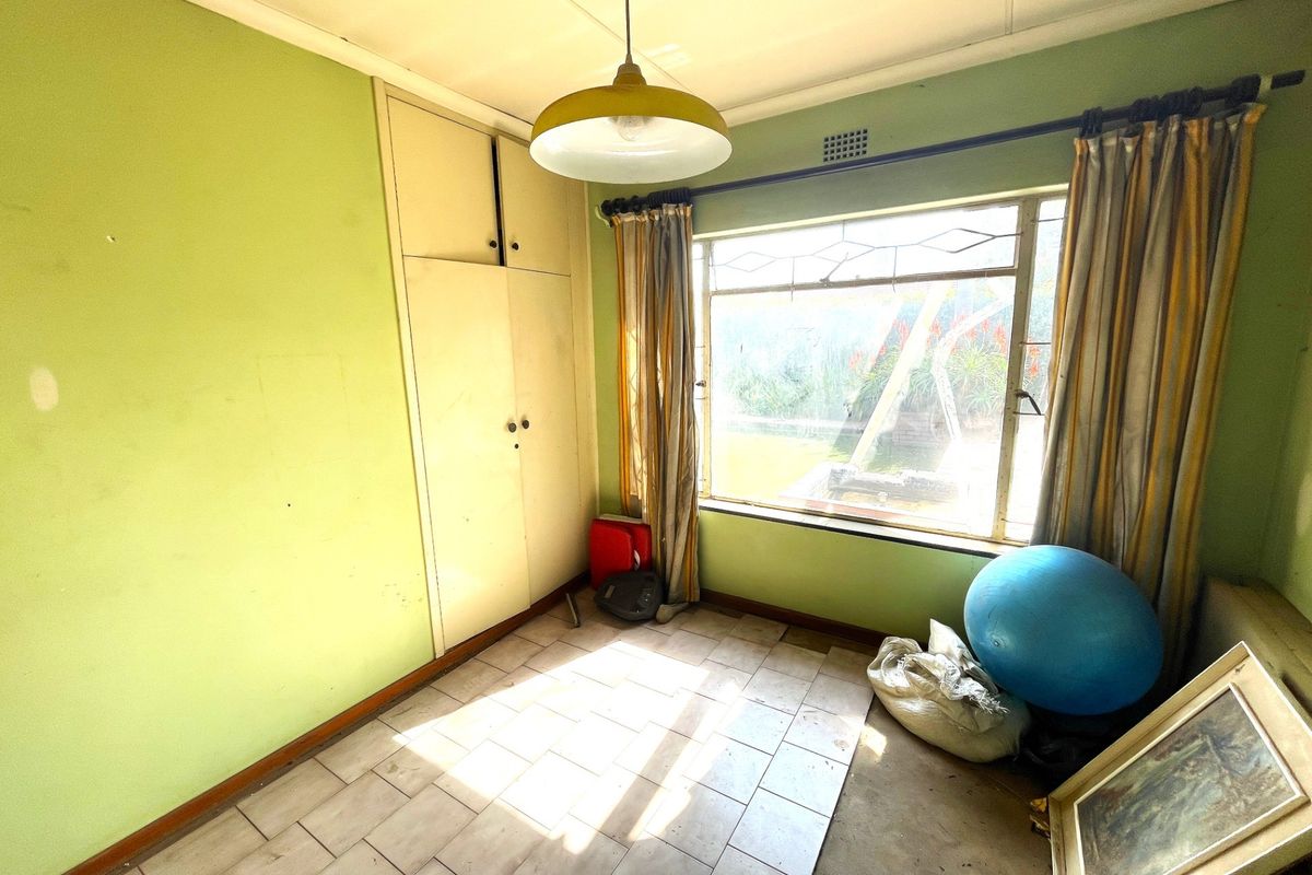 A bedroom featuring built-in cupboards, tiled flooring, and a large window providing natural light.