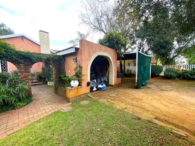 Rear garden area featuring a brick-arched walkway, covered storage structure, and established landscaping with a mix of paved and natural ground surfaces.