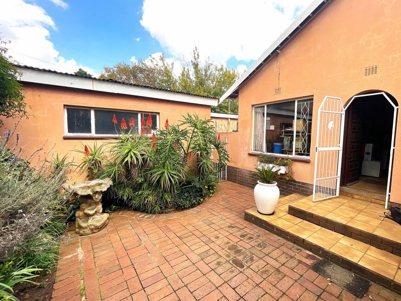 A paved rear courtyard area featuring brick flooring, established garden beds, and direct access to the main house via a tiled entrance.