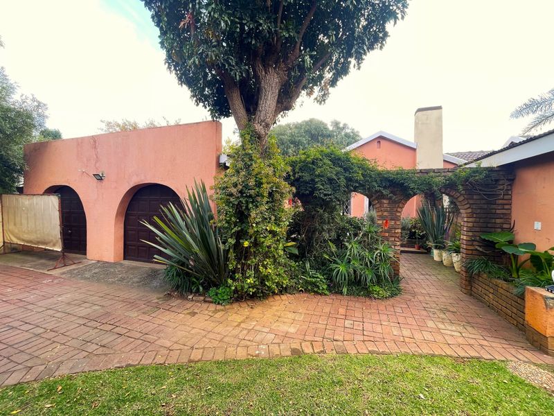 Exterior view of the property featuring a brick-paved courtyard, arched garage entrances, and a covered brick walkway with established garden landscaping.