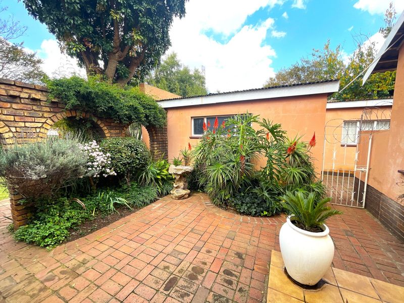 A private rear courtyard featuring brick paving, established garden beds, and a decorative brick archway, providing a quiet outdoor space.