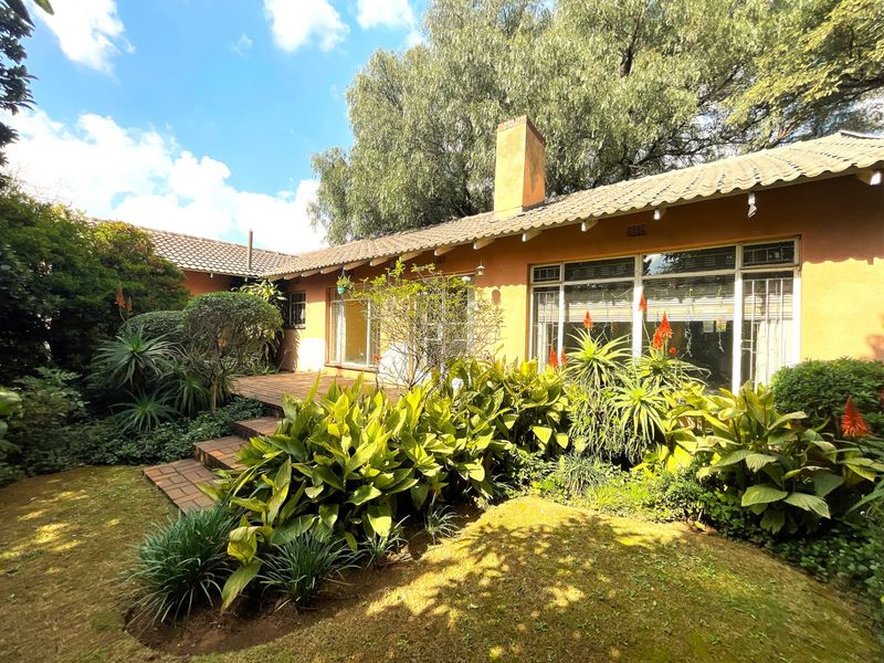 Rear view of the house featuring a brick patio, established garden landscaping, and large windows with metal frames.