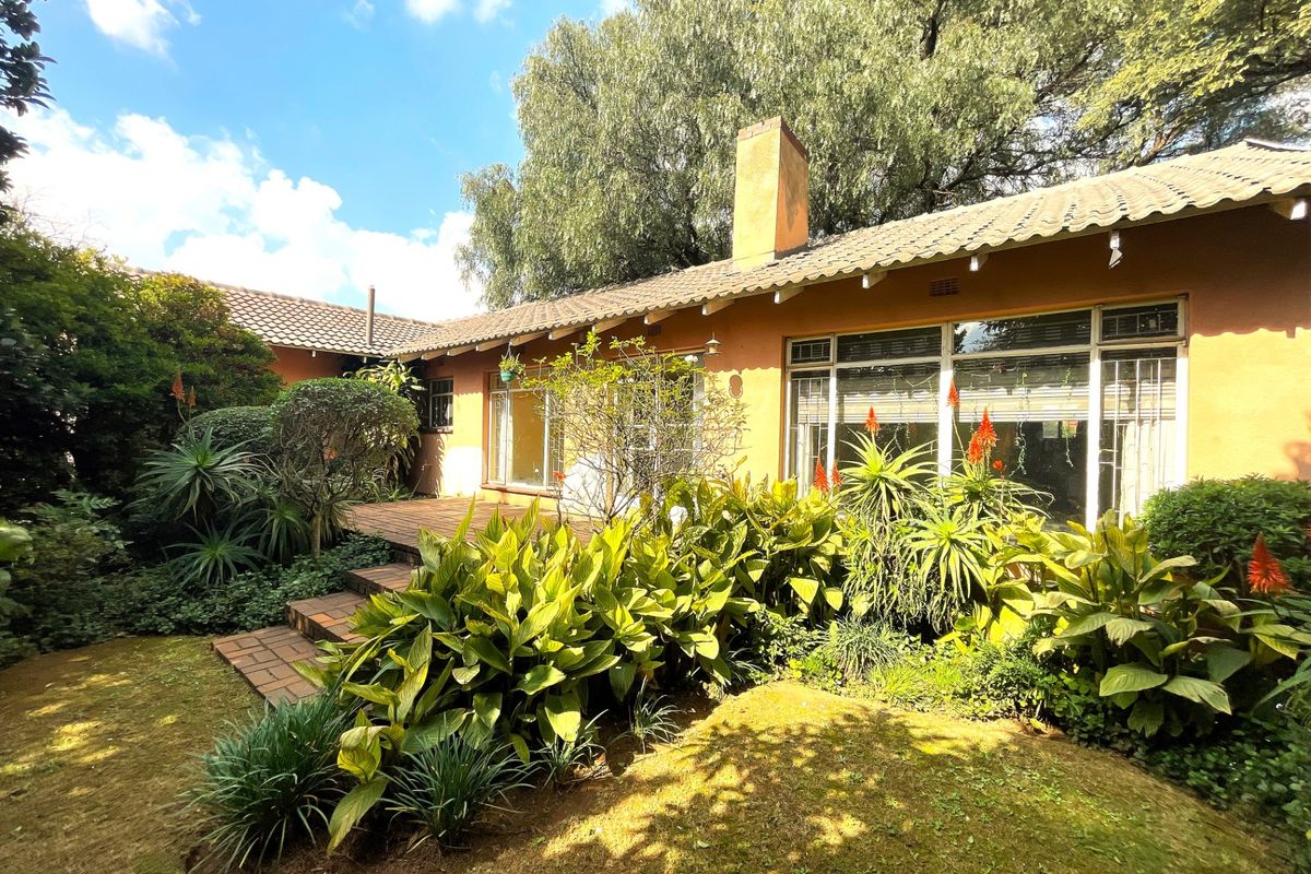 Rear view of the house featuring a brick patio, established garden landscaping, and large windows with metal frames.