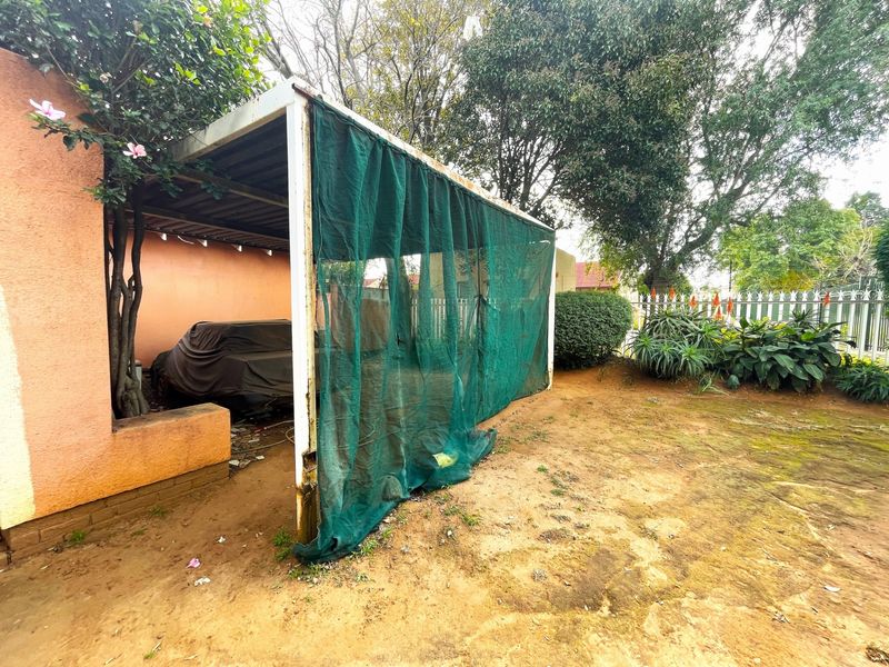 An outdoor carport structure featuring a metal frame and shade cloth covering, situated in a garden area with natural ground.