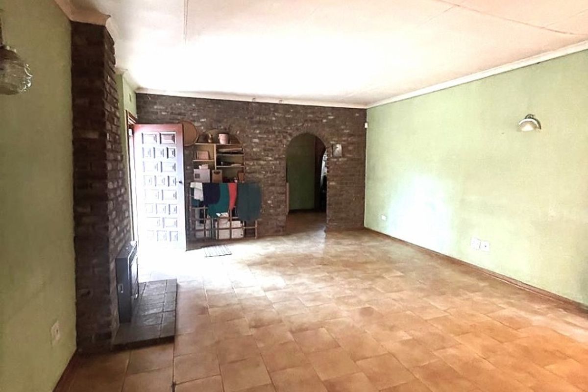Spacious living room featuring tiled flooring, an exposed brick fireplace, and an arched entryway, offering a blank canvas for renovation.