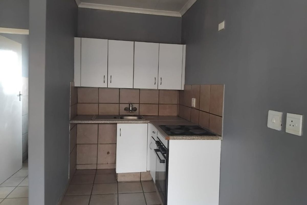 Compact kitchen featuring white cabinetry, a built-in stove with oven, tiled backsplash, and tiled flooring.