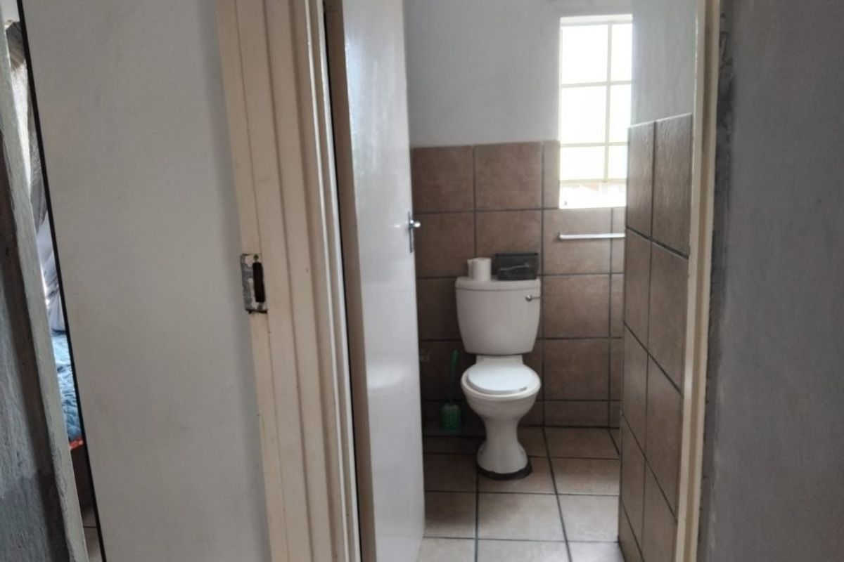 A compact bathroom featuring a standard toilet, tiled flooring, and partial wall tiling, viewed from the adjacent hallway.