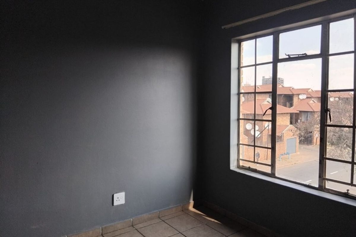 An empty bedroom featuring dark grey painted walls, tiled flooring, and a large metal-framed window overlooking the street.
