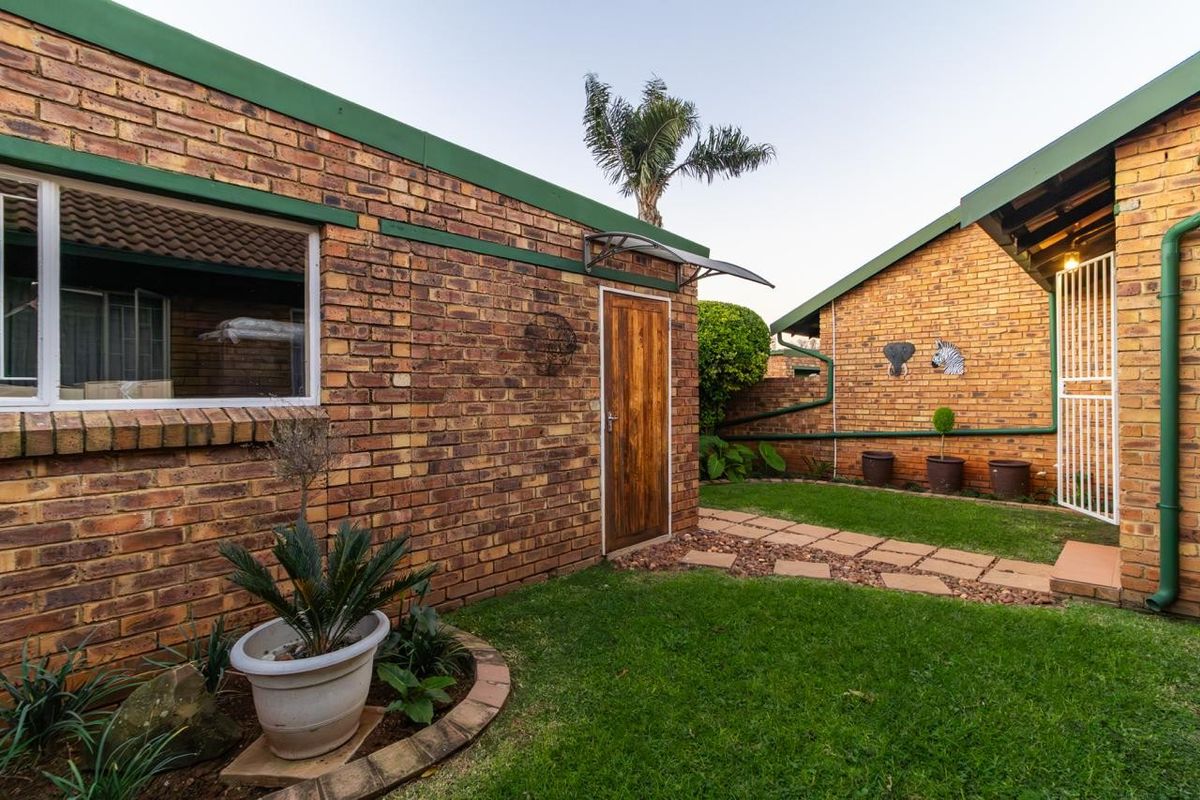 A private rear courtyard featuring a brick-walled exterior, a paved walkway, and a well-maintained lawn area.