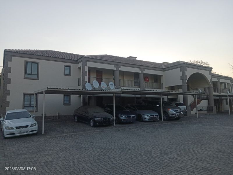 Exterior view of a multi-story apartment complex featuring a covered carport area, paved driveway, and upper-level balconies.