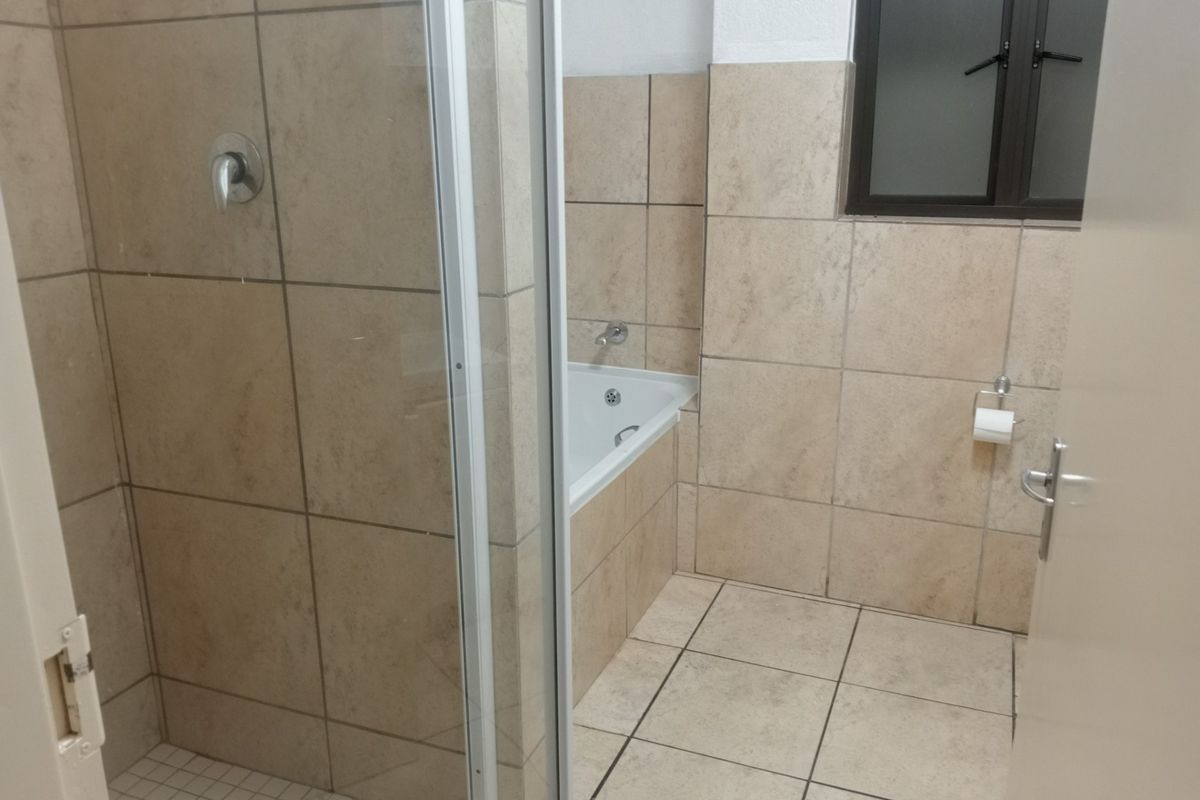A functional bathroom featuring a separate shower enclosure, a built-in bathtub, and neutral ceramic tiling throughout.